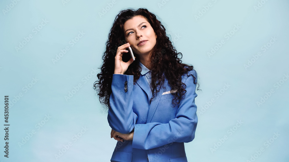 brunette woman smiling and looking away while talking on mobile phone isolated on blue brunette woman smiling and looking away while talking on mobile phone isolated on blue