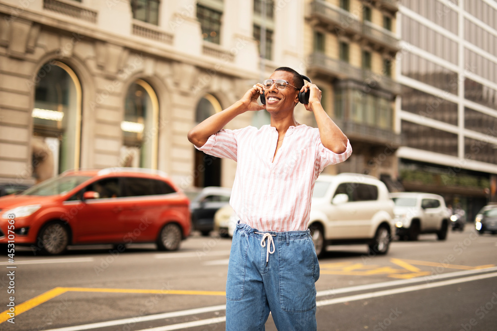 Cheerful guy listening the music with the headphones. Young african man walking through the city