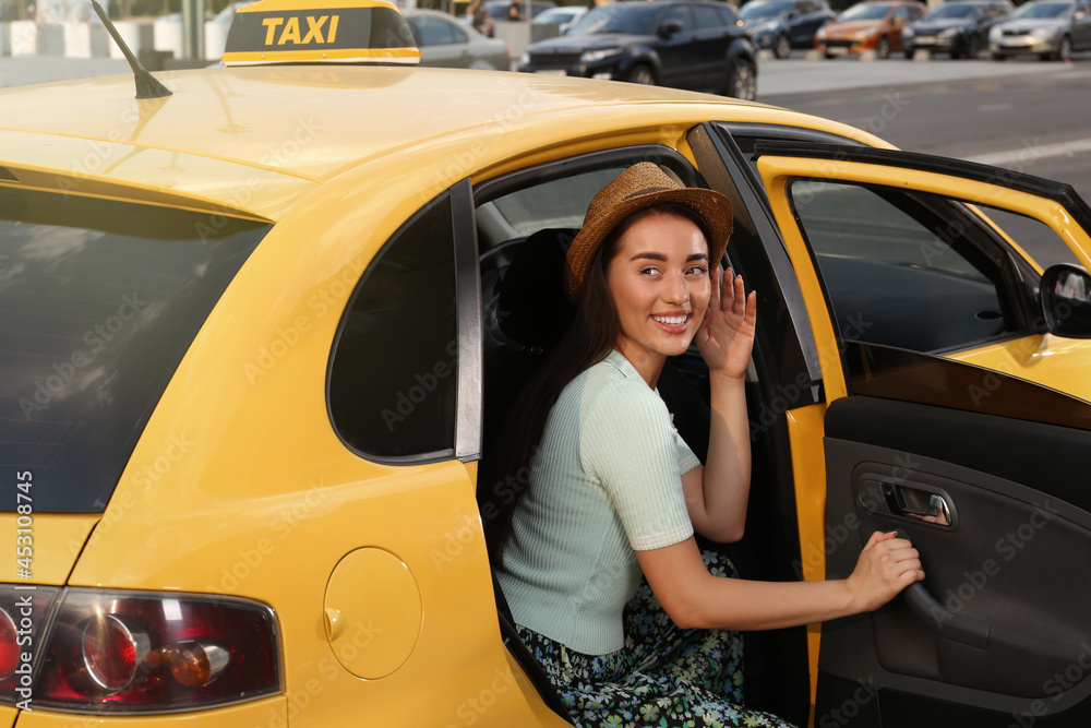 Naklejka premium Beautiful young woman getting out of taxi on city street