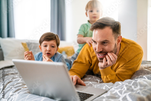 Handsome man and their children are using a laptop together on the bed at home