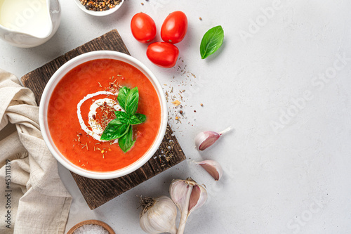 Tomato soup with cream and fresh basil on a gray background. Top view, copy space.