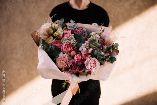 Very nice young woman holding big and beautiful bouquet of fresh roses, carnations, eucalyptus, protea flowers in pink colors, cropped photo, bouquet close up