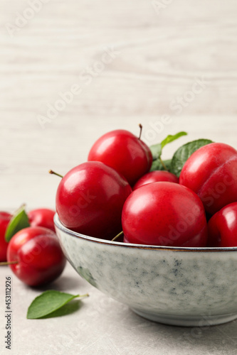 Delicious ripe cherry plums with leaves on light table, closeup