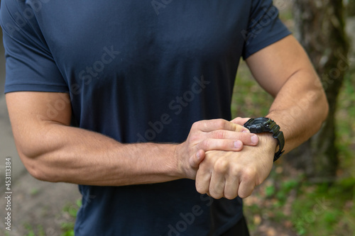 A man looks at the clock time in the park outdoors, around the forest, oaks green grass young enduring athletic athlete. active sport nature, fitness trail fit wellness motion, woods wellbeing. Autumn