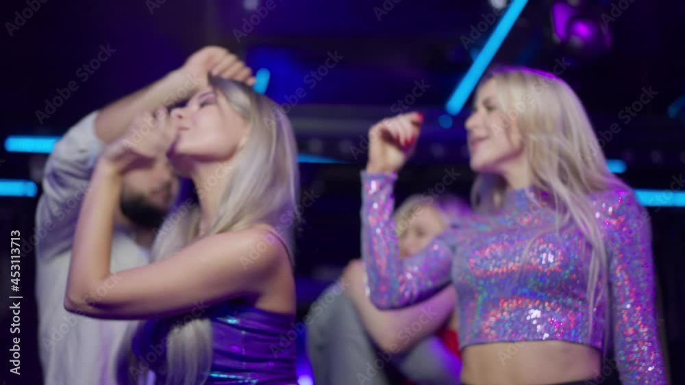 Side view of slim happy young woman dancing in night club singing having fun with group of friends. Slender confident beautiful Caucasian millennial moving to music on dance floor Side view of slim happy young woman dancing in night club singing having fun with group of friends. Slender confident beautiful Caucasian millennial moving to music on dance floor