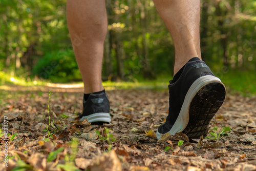 Legs in sneakers close up athlete runs in the park outdoors, around the forest, oak trees green grass young enduring athletic athlete runner exercise, fitness jogger athletic recreation marathon