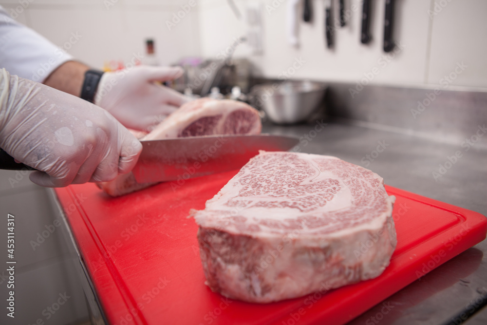 Close up of a marbled beef raw meat on cutting board, chef working on background Close up of a marbled beef raw meat on cutting board, chef working on background