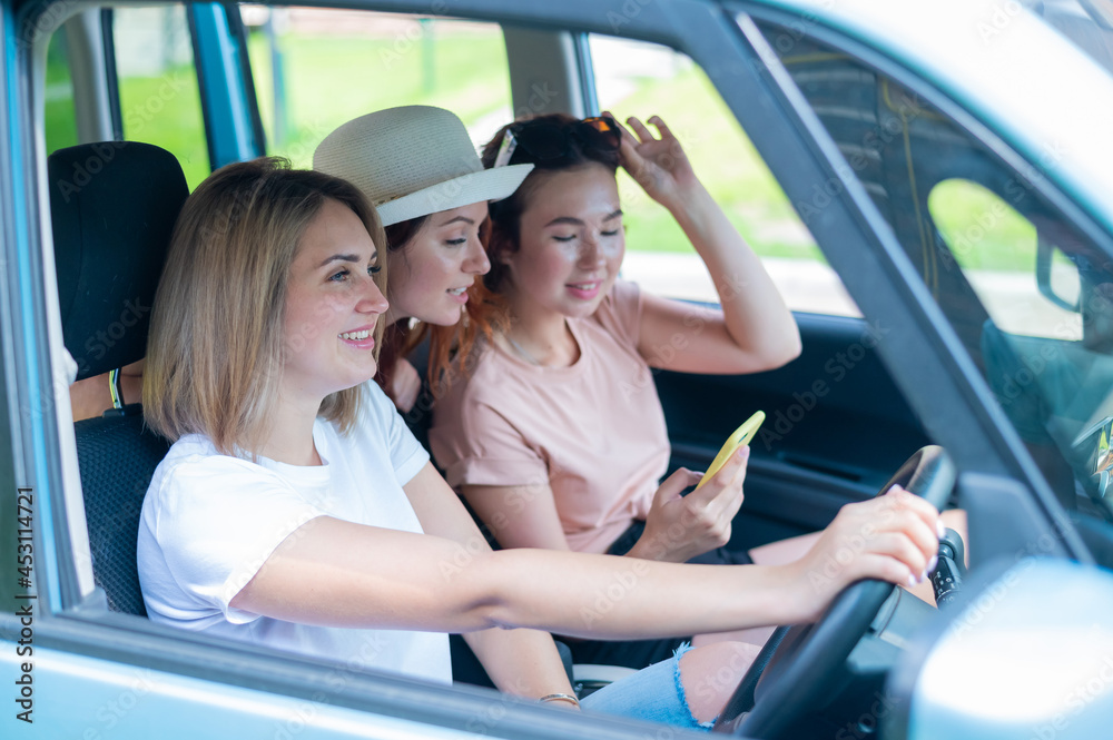 Three happy girlfriends go on a trip. Women Ride in the car, look at the phone and laugh. Three happy girlfriends go on a trip. Women Ride in the car, look at the phone and laugh.