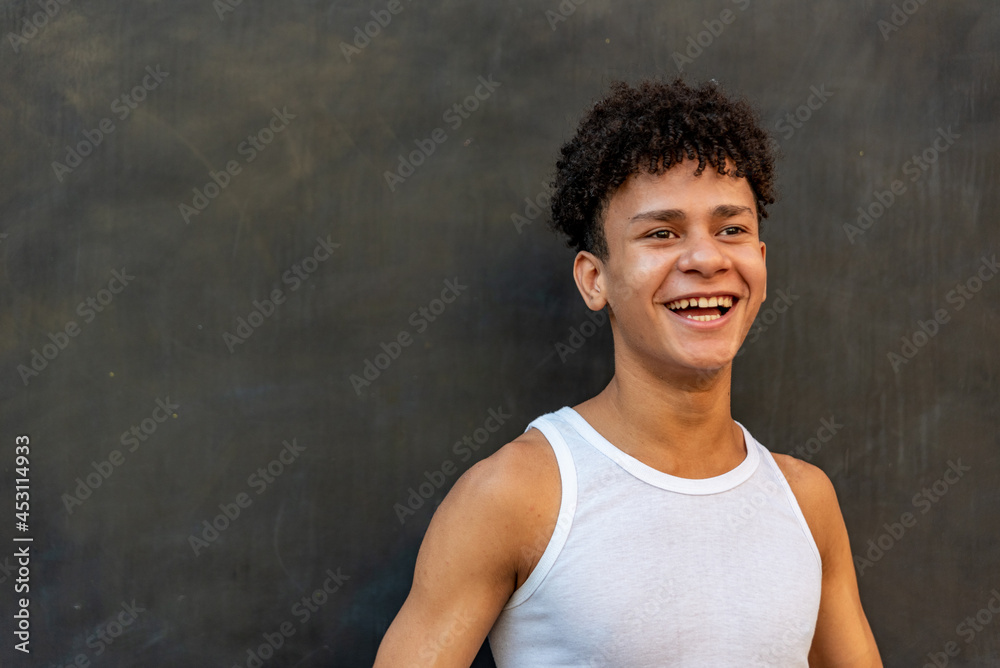 Afro latin male teenager smiling against a black wall