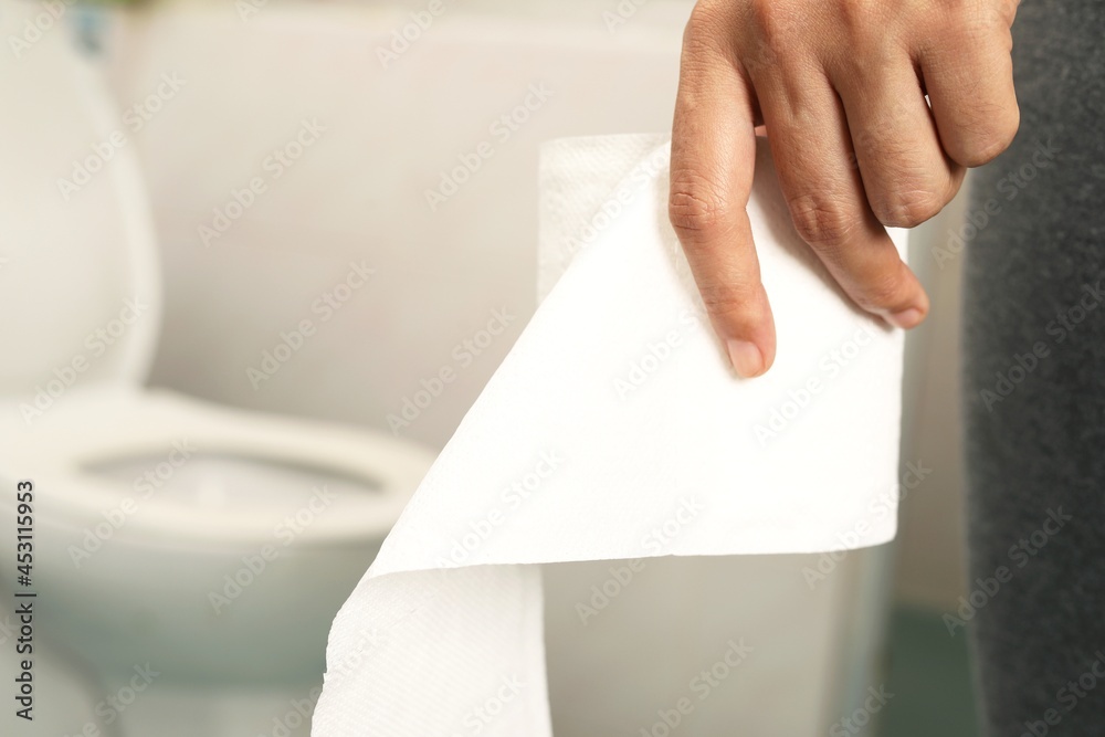 A woman in gray trousers holds toilet paper in the bathroom. A woman in gray trousers holds toilet paper in the bathroom.