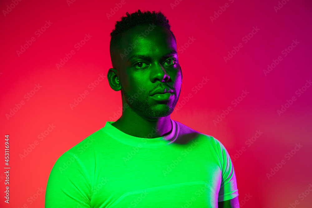 Creative image of African young man in casual clothes isolated on red color studio background in neon light, filter. Concept of human emotions, facial expression, youth, feelings, ad. Creative image of African young man in casual clothes isolated on red color studio background in neon light, filter. Concept of human emotions, facial expression, youth, feelings, ad.