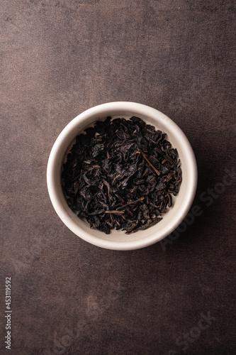 selective focus, natural black leaf tea. brewing in a clay bowl. vertical angle, macro. on a dark background. for menus and cafes