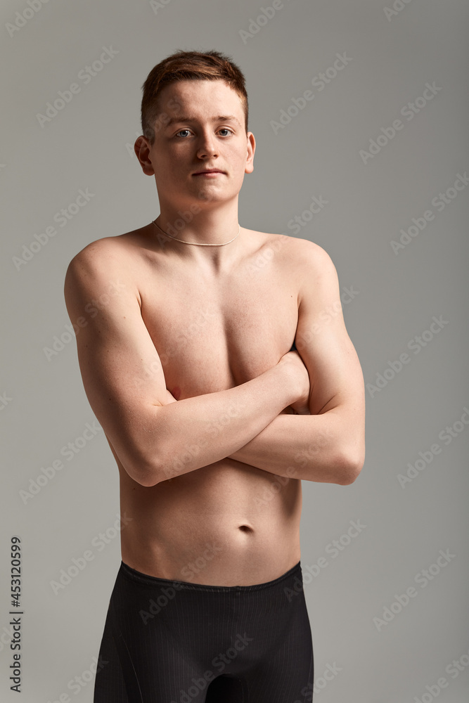 Young attractive swimmer in excellent physical shape in purple swimming shorts, on a gray background, copy space