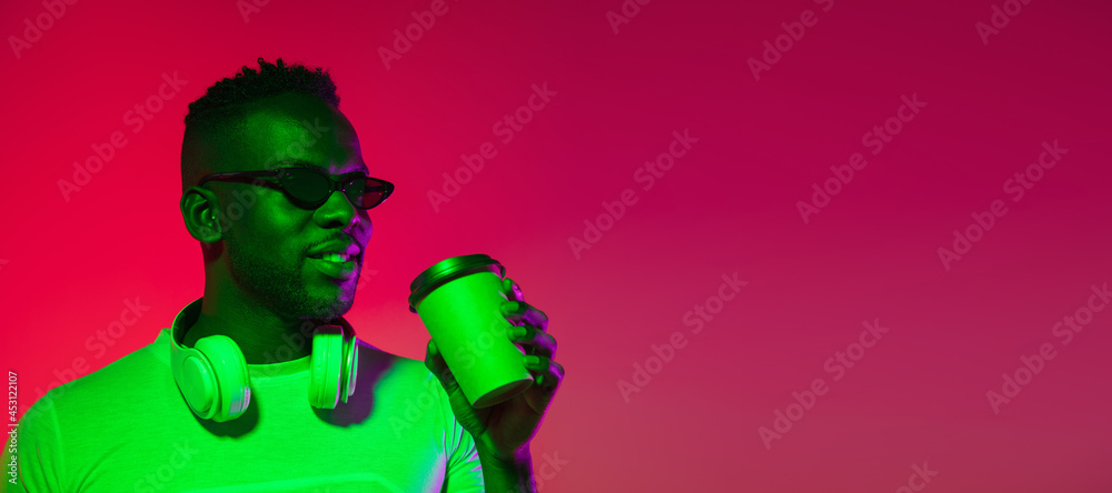 Creative image of African young man in casual clothes isolated on red color studio background in neon light, filter. Concept of human emotions, facial expression, youth, feelings, ad. Creative image of African young man in casual clothes isolated on red color studio background in neon light, filter. Concept of human emotions, facial expression, youth, feelings, ad.