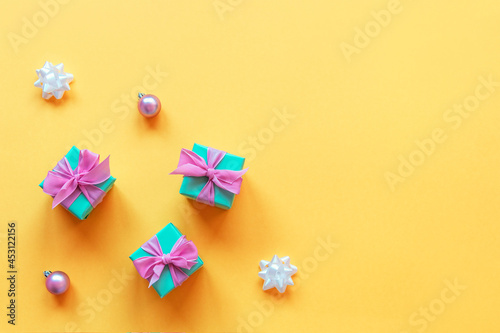 Three turquoise present boxes with pink bows, Christmas balls and baubles on yellow background. Top view, flat lay, copy space