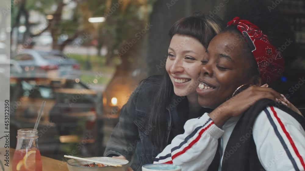 Slowmo shot through window of cafe happy queer couple laughing and chatting while enjoying their date Slowmo shot through window of cafe happy queer couple laughing and chatting while enjoying their date
