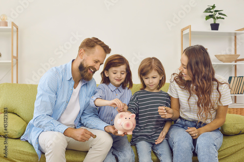 Canvas-taulu Happy family sitting on cozy sofa at home and putting coins inside piggy bank
