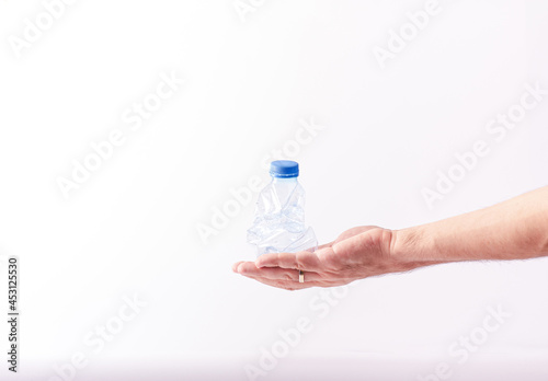 An anonymous hand is holding an used plastic water bottle, recycleable item concept; includes copy space photo