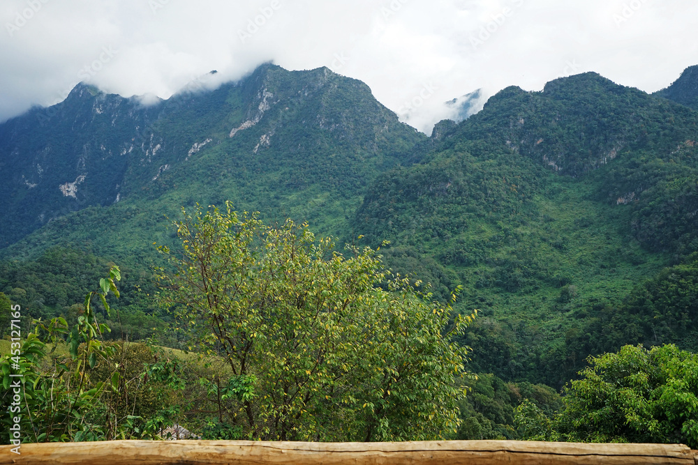 View of high green mountain and cloudy blue sky from wooden balcony