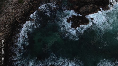 Slow rise and spin over ocean with waves crashing over rocks on the coast