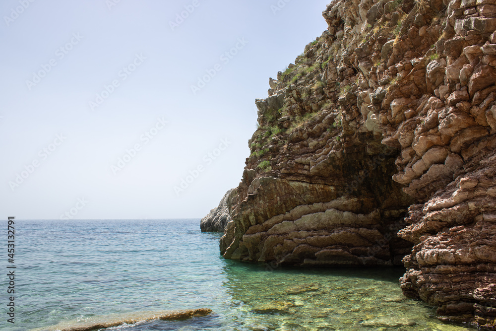 Naklejka premium Rocky seaside coast. Boulders are standing in the beautiful water. Group of large stones against the blue sky. Big stone on the background of the sea.