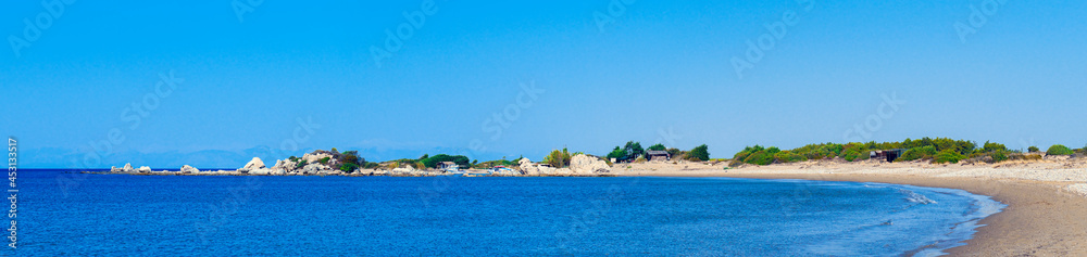 Panorama of bay coastline with dunes, small houses and boats. Sand dunes with green bushes and rocks. Panoramic view of sandy beach in the bay.
