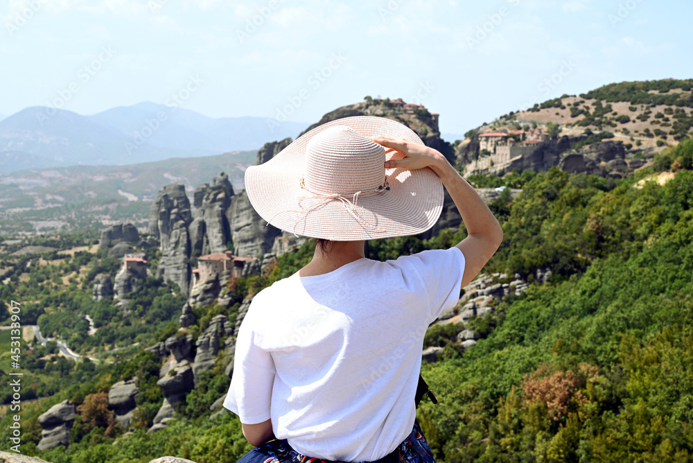 Fille assise de dos à chapeau rose poudré et t-shirt blanc contemplant l'horizon de montagnes rocailleuses