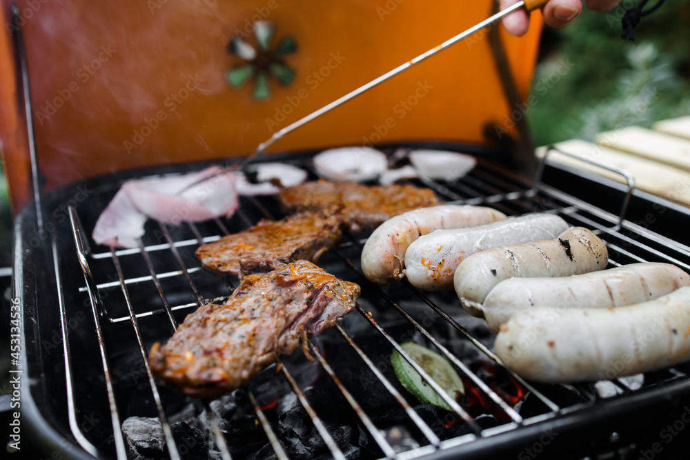 View of the grill with beef steaks, sausages and vegetables. meat and sausages are grilled on the grill. Spend time with your family at the grill. Social meetings, friends. Red grill with kindling