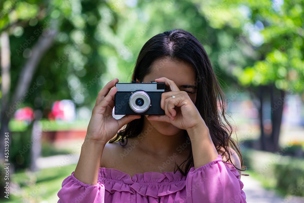 Woman in a pink dress taking photographs with a vintage film camera in a park