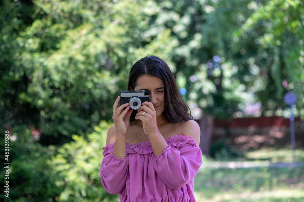 Woman in a pink dress taking photographs with a vintage film camera in a park