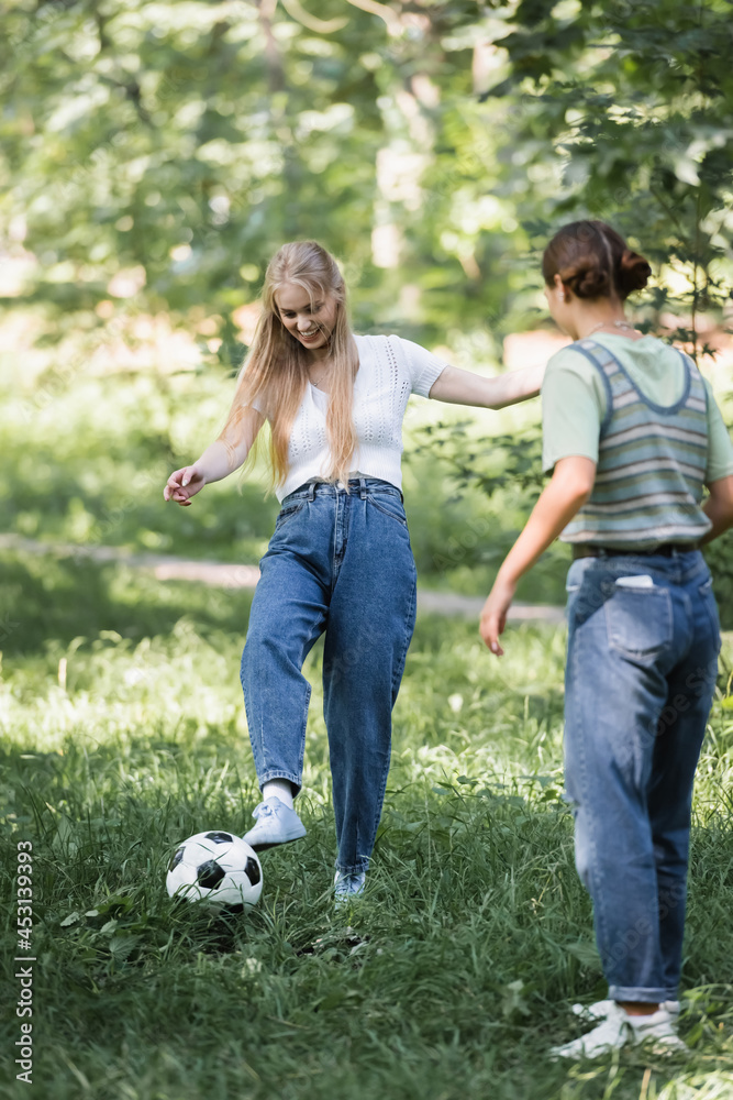 Teen girl playing football with blurred friend in park