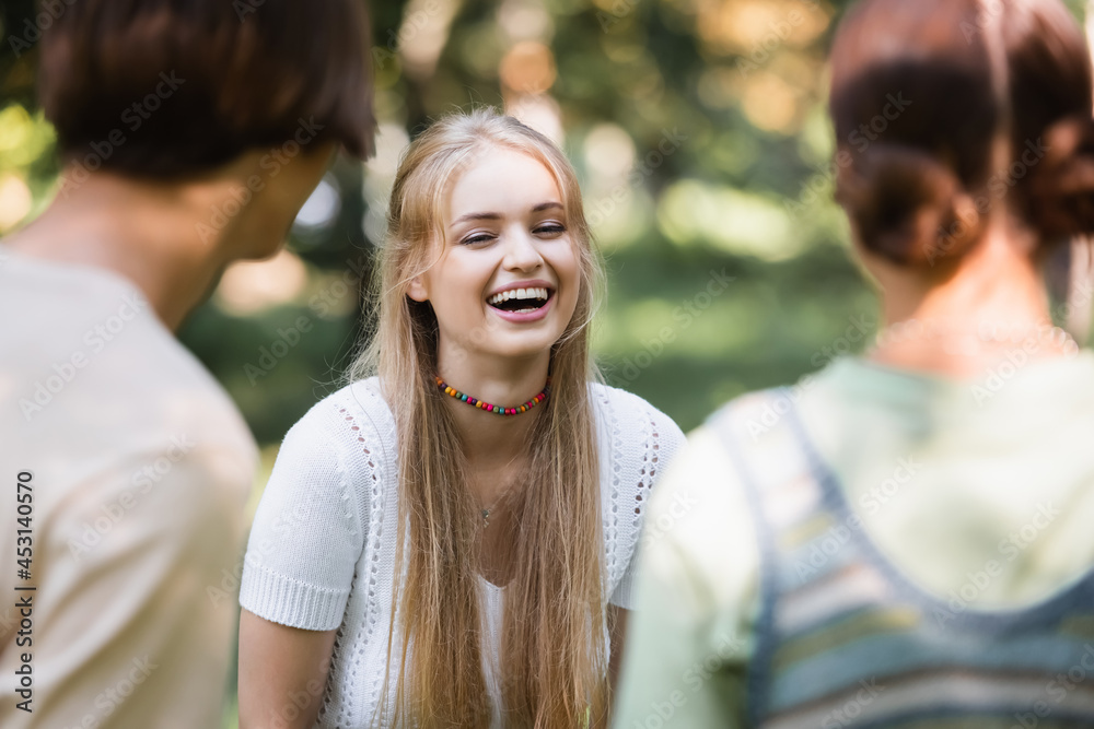 Cheerful teenager standing near blurred friends outdoors Cheerful teenager standing near blurred friends outdoors