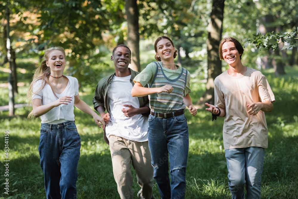 Happy multiethnic teenagers running on grass in park Happy multiethnic teenagers running on grass in park