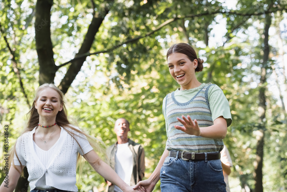 Smiling girl holding hand of teen friend in park Smiling girl holding hand of teen friend in park
