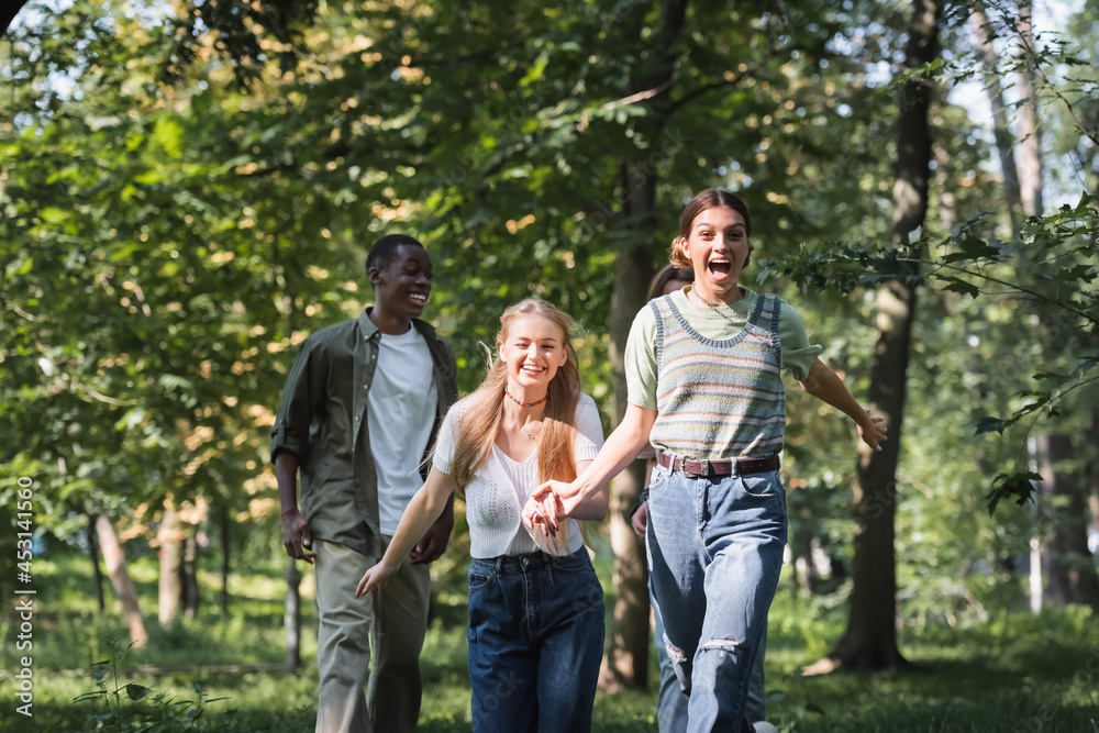 Cheerful teen girls running near multiethnic friends in park