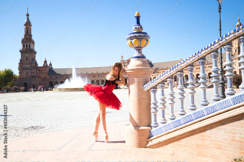 ballet dancer with red tutu leaning on a park railing in seville. The dancer makes different postures and stretches on the railing. Classical ballet concept. - obrazy, fototapety, plakaty 