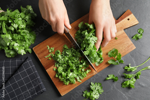 Woman cutting fresh green cilantro at black table, top view photo