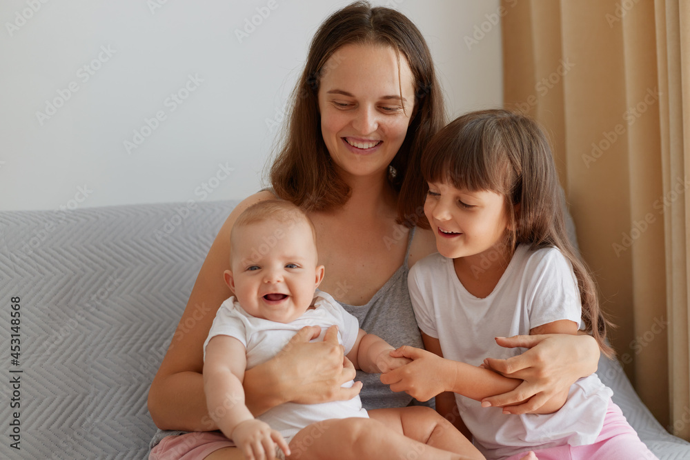 Happy smiling woman sitting with her children on sofa, family spending time indoor at home, laughing happily, talking, people wearing casual style clothing. Happy smiling woman sitting with her children on sofa, family spending time indoor at home, laughing happily, talking, people wearing casual style clothing.