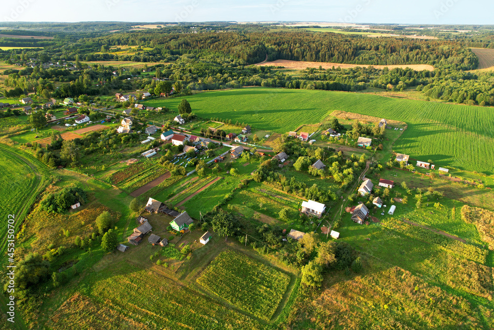 Top view of the village with wooden houses in wild among the forest and field. Aerial view of country house in countryside. Roofs of suburban homes. Housing outside the city in an ecological area.