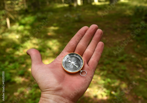 Compass in hand at forest. Tourist compass for orientation on the terrain. Magnetic declination сalculator. Historical explorer help. Map reading and land navigation concept. Orient on maps