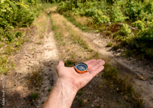 Compass in hand at road in the forest. Tourist compass for orientation on the terrain. Magnetic declination сalculator. Map reading and land navigation concept. Orient on maps