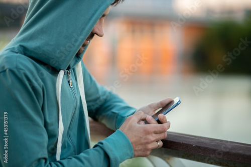 Hooded man using smartphone outdoors
