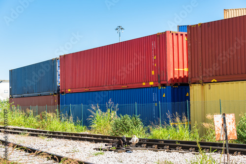 Stack of colourful containers along railway tracks in a freight terminal on a sunny summer day.