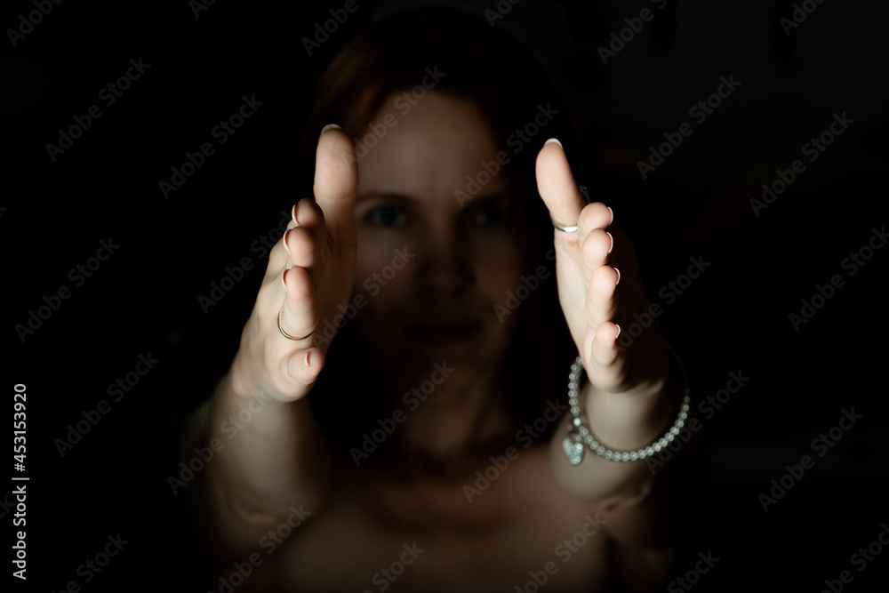 Outstretched illuminated hands of a woman from the darkness.