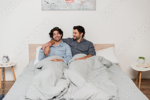 cheerful gay couple smiling while chilling in bed