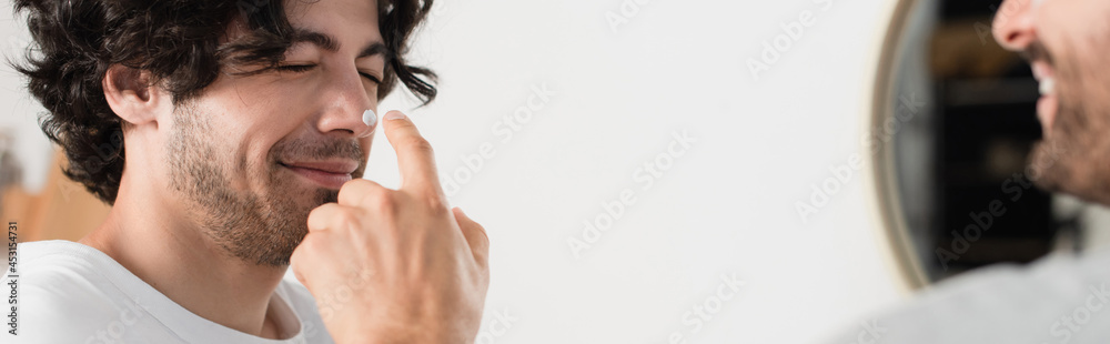 cheerful and blurred man applying cream on nose of smiling boyfriend, banner cheerful and blurred man applying cream on nose of smiling boyfriend, banner