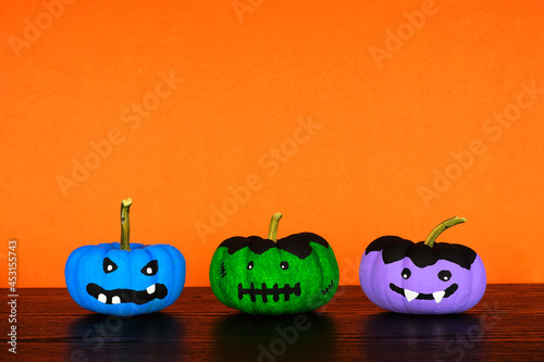 Painted Halloween pumpkins on a black shelf against an orange background. Monster, frankenstein and vampire. photo