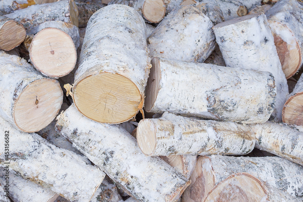 Lots of frozen sawn birch logs. The firewood is sawn and covered with snow. The logs lie chaotically and are piled up in one heap. The image can be used as a texture or background. Lots of frozen sawn birch logs. The firewood is sawn and covered with snow. The logs lie chaotically and are piled up in one heap. The image can be used as a texture or background.