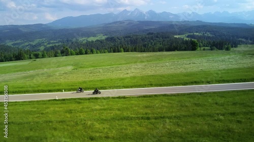 Aerial view of mountain road and two motorcyclists are driving on an empty road. In the background wide Tatra mountains range. Concept: Vacations in mountains, road trip, traveling.