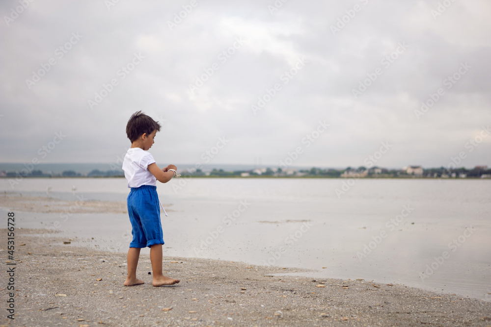 tanned child boy in blue shorts and a white T-shirt walks barefoot on the lake in summer